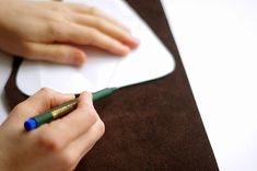 a person writing on a piece of paper with a green marker and pen in their hand