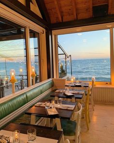 an empty restaurant with tables and chairs overlooking the ocean at sunset or sunrise, in front of large windows that look out onto the water