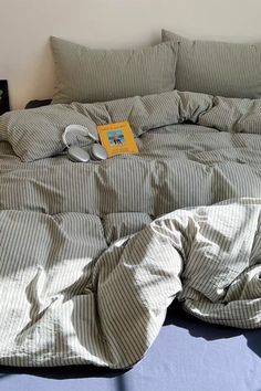 an unmade bed with two pillows and a book on the pillowcase next to it