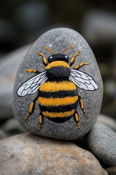 a yellow and black bee painted on top of a rock next to some gray rocks