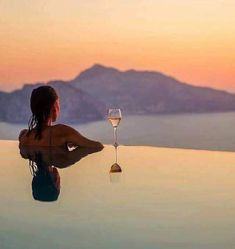 a woman sitting at the edge of a pool with a glass of wine in front of her