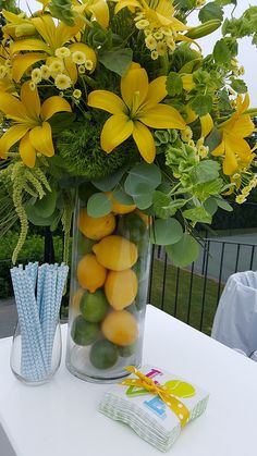 a vase filled with yellow flowers and lemons on top of a table next to two strawberries