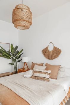 a bed with pillows and blankets on top of it in a bedroom next to a potted plant