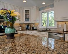 a large kitchen with granite counter tops and white cabinetry, along with a green vase filled with flowers