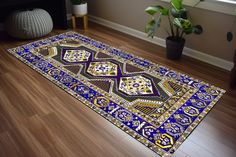 a blue and yellow rug on the floor next to a potted plant in a room