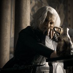 an old woman sitting at a table with her hands on her face and looking off into the distance