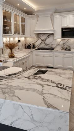 a large kitchen with marble counter tops and white cabinetry, along with stainless steel appliances