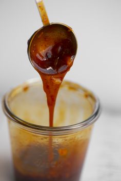 a spoon full of caramel sauce being poured into a jar