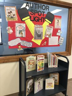 a book stand with books on it in front of a bulletin board