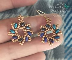 a pair of blue and gold earrings on someone's finger with the words beading butterfly