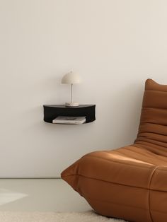 a brown leather chair sitting in front of a white wall with a black shelf on it