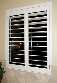 an open window with white shutters and tiled walls in front of the window is a potted plant