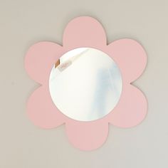 a pink flower shaped mirror sitting on top of a white table next to a wall