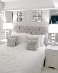 a white bed with four pillows and two lamps on either side of the headboard