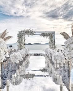 an outdoor wedding setup with white flowers and candles on the aisle, overlooking the ocean