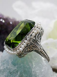 Simulated Green Peridot Ring Description Rectangle Seed Pearl Leaf Design#234 MADE TO ORDER This is a stunning Victorian reproduction in sterling silver filigree with a simulated green peridot rectangle stone... The stunning stone is 18mm by 13mm...The ring sits 21mm NS by 19mm EW... The inside of the band is marked 925 for sterling. Notice the beautiful craftsmanship of the silver filigree setting and band. The small natural pearls are 2mm wide... The ring is 9mm off the finger This is an ornat Luxury Green Pearl Ring Fine Jewelry, Green Pepper Rings, Leaf Filigree, Filigree Pendant Necklace, Antique Style Rings, Pearl Design, Green Gems, Peridot Gemstone, Peridot Ring