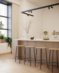 a kitchen with three stools and an island in front of a window that has potted plants on it