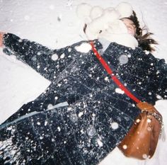 a woman is laying in the snow with her hand on her head and wearing a coat