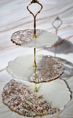 three tiered trays with sprinkles and gold handles on marble surface