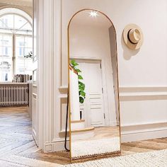 a large mirror sitting on top of a wooden floor next to a white wall with a plant in it