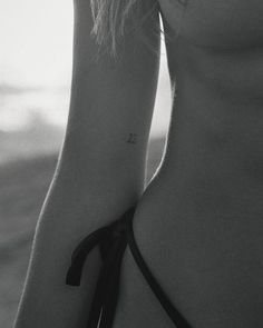 a black and white photo of a woman's back with a small tattoo on her left arm