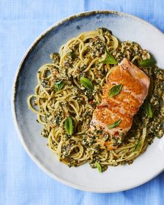 a white plate topped with pasta and salmon on top of a blue table cloth next to a fork