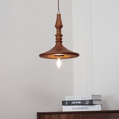 a wooden light fixture hanging from the ceiling above a dresser with books on it and a white wall in the background