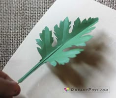 a person is holding a green leaf on top of a piece of paper that has been cut out