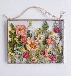 a glass frame with flowers and greenery hanging on the wall above it is a string