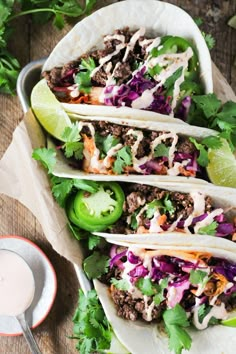 three tacos with meat, lettuce and sauce on a plate next to a small bowl