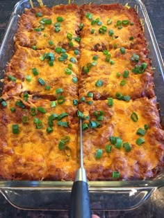 a casserole dish with cheese and green onions on it being cut into squares