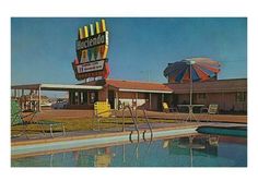 an old motel with a swimming pool in the foreground and umbrellas over it