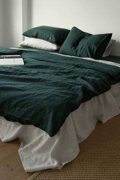 a bed with green sheets and pillows in a white room next to an open window