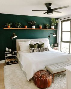 a bedroom with dark green walls and white bedding, potted plants on the wall