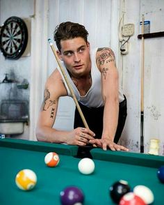 a man with tattoos leaning over a pool table