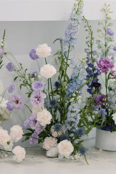 three white vases filled with purple and white flowers next to each other on a table