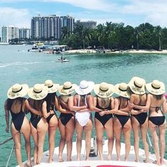 a group of women in bikinis and hats standing on a boat looking at the water