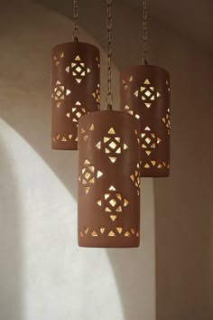 three brown lamps hanging from chains in a room with white walls and shadows on the wall