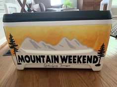 a cooler with the words mountain weekend on it sitting on a wooden floor in front of a couch