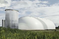 two large white tanks sitting next to each other on a lush green field under a cloudy blue sky