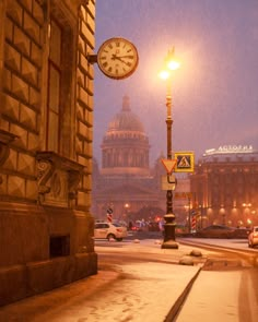 a clock on a pole in the middle of a snowy street with cars driving by