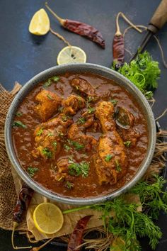 a bowl filled with chicken curry and garnished with cilantro, parsley and lemon wedges