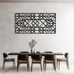 a dining room table with chairs and a vase on top of it, in front of a wall sculpture