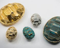 four different colored metal objects on a white surface with gold and green designs in the middle