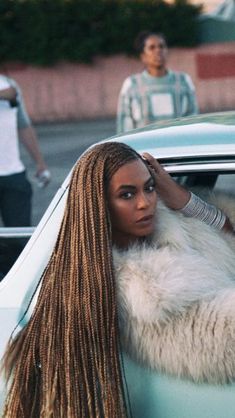 a woman with long hair leaning on the hood of a car in front of another man