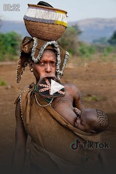 a woman carrying a basket on her head with other items on her shoulders and an arrow in her mouth