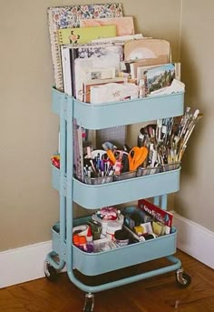 a blue cart filled with lots of crafting supplies on top of a hard wood floor