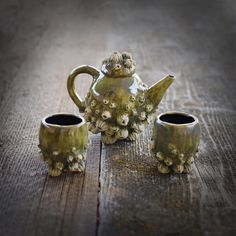 a tea pot and two cups sitting on a wooden table next to each other with flowers growing out of them