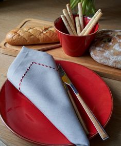 a red plate topped with a napkin next to a bowl filled with bread