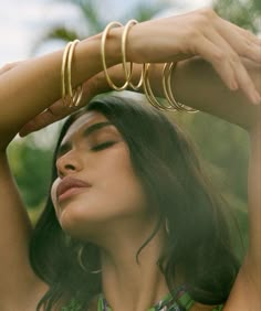 a woman with her hands on her head wearing gold bracelets and ring necklaces